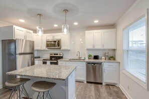 A modern kitchen with white cabinets, granite countertops, stainless steel appliances, pendant lighting, and a large window. - Memory Maker | Chic 1BR Retreat (Nashville)