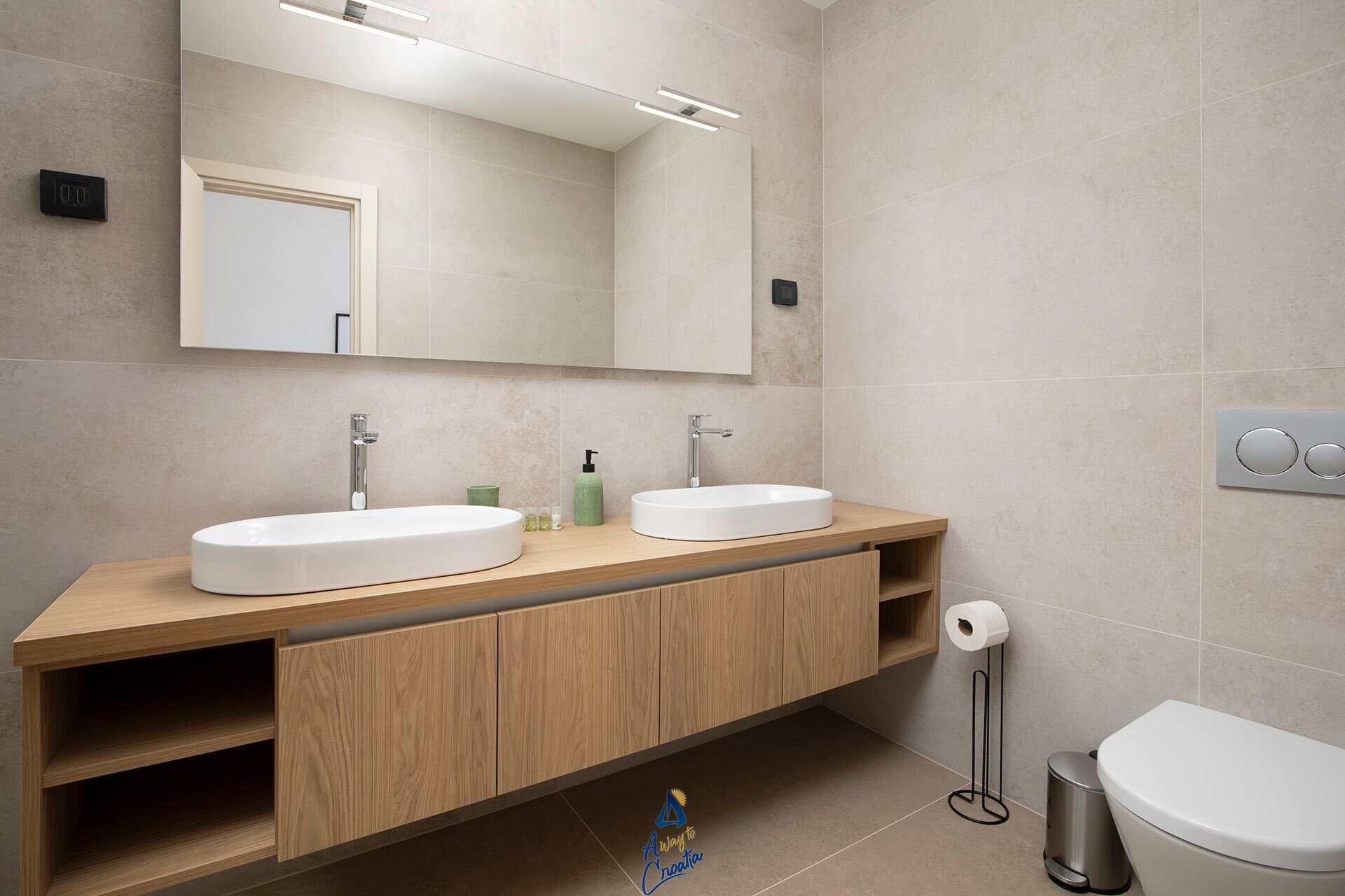 Une salle de bain moderne avec un double vasque, un meuble-lavabo en bois, un grand miroir et des toilettes.
