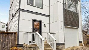 A two-story residential building with a white exterior, a front entrance, a visible garage door, and a small front yard with a wooden fence and some shrubs. - 15 Min to Broadway - Fenced Yard - Family Friendly (Nashville)