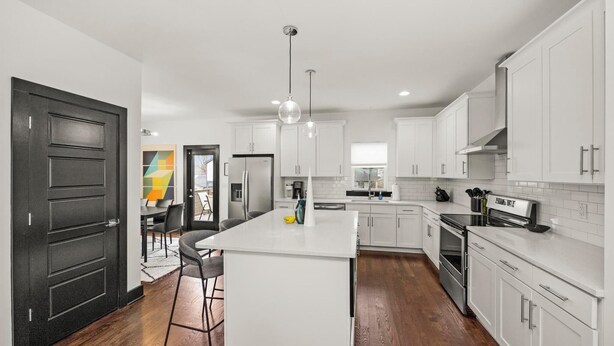 A modern kitchen with white cabinetry, a central island, and a dark wooden floor. - 15 Min to Broadway - Fenced Yard - Family Friendly (Nashville)