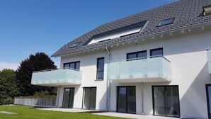 Et moderne hus i to etager med fladt tag, store vinduer og en balkon med gelændere i glas.