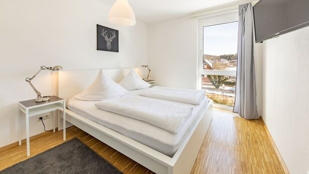 Et moderne soveværelse med en stor seng, sengeborde, et skrivebord og et vindue med udsigt.