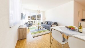 En moderne stue med sofa, sofabord og spisebord. Store vinduer giver udsigt til det fri.