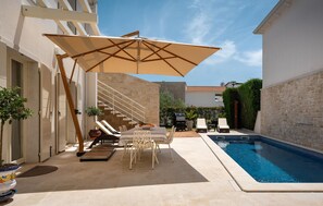 Un espace aménagé au bord de la piscine, comprenant une chaise longue, un parasol et un barbecue.