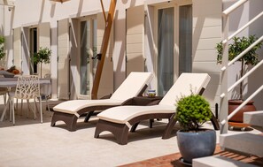 Un espace extérieur ensoleillé, aménagé avec deux fauteuils de jardin, une table avec des chaises et des plantes en pot.