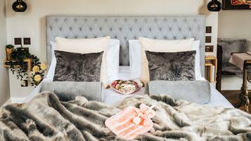 A bedroom with a tufted headboard, two white pillows, two dark pillows, a floral throw, and a pink towel.