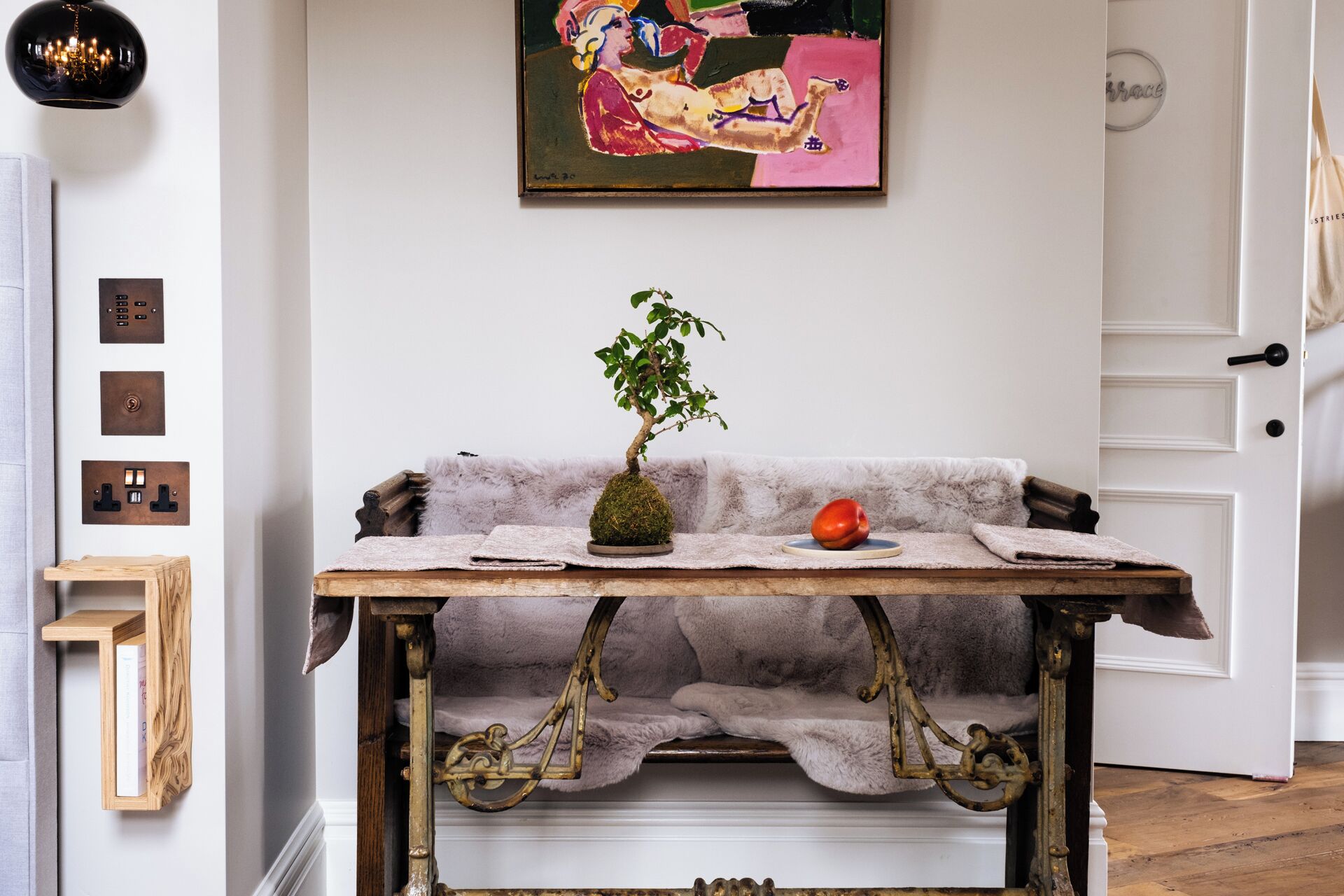 A room with a vintage wooden table, a potted plant, and a painting on the wall.