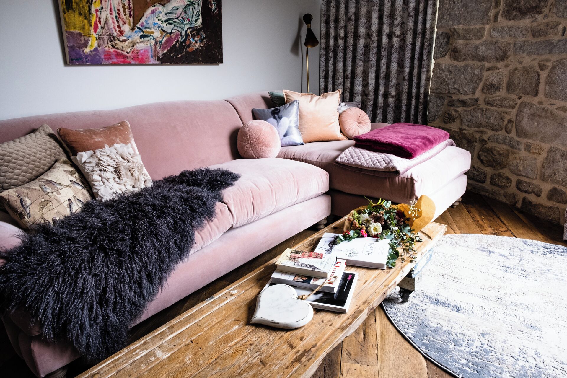 A cozy living room with a pink sofa, a wooden coffee table, and a stone wall.