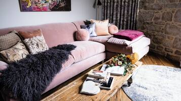A cozy living room with a pink sofa, a wooden coffee table, and a stone wall.