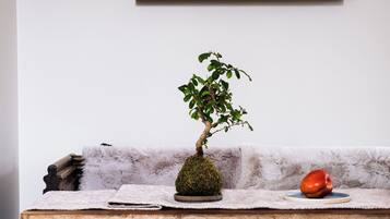 A small bonsai tree on a table with a white cloth, a red apple, and a wooden sculpture.