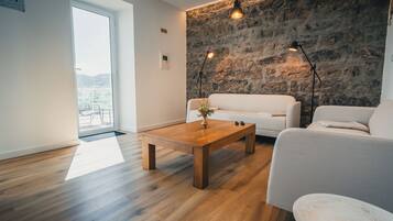 A modern interior with a stone wall, a wooden coffee table, and two white sofas.