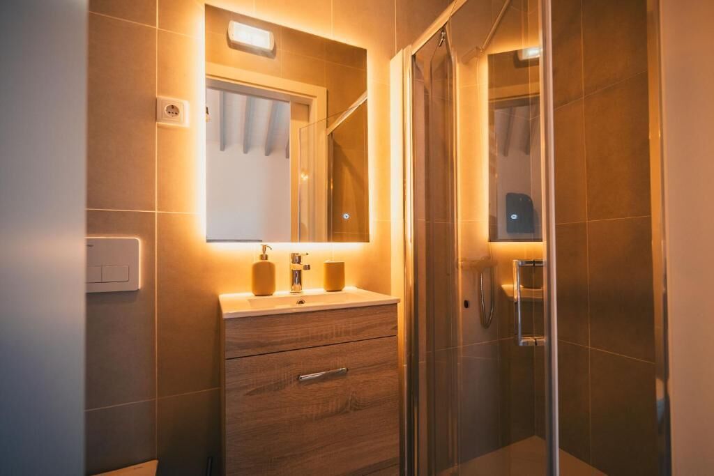 Een moderne badkamer met een douchecabine van glas, een houten wastafelmeubel met spiegel en een wandlamp.