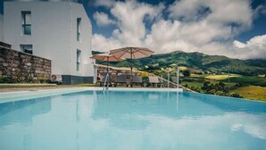 A modern building with a pool, outdoor seating, and a view of green hills. - Benilde Village House (Povoacao)