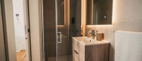 A modern bathroom with a glass shower enclosure, a wooden vanity, and a large mirror.