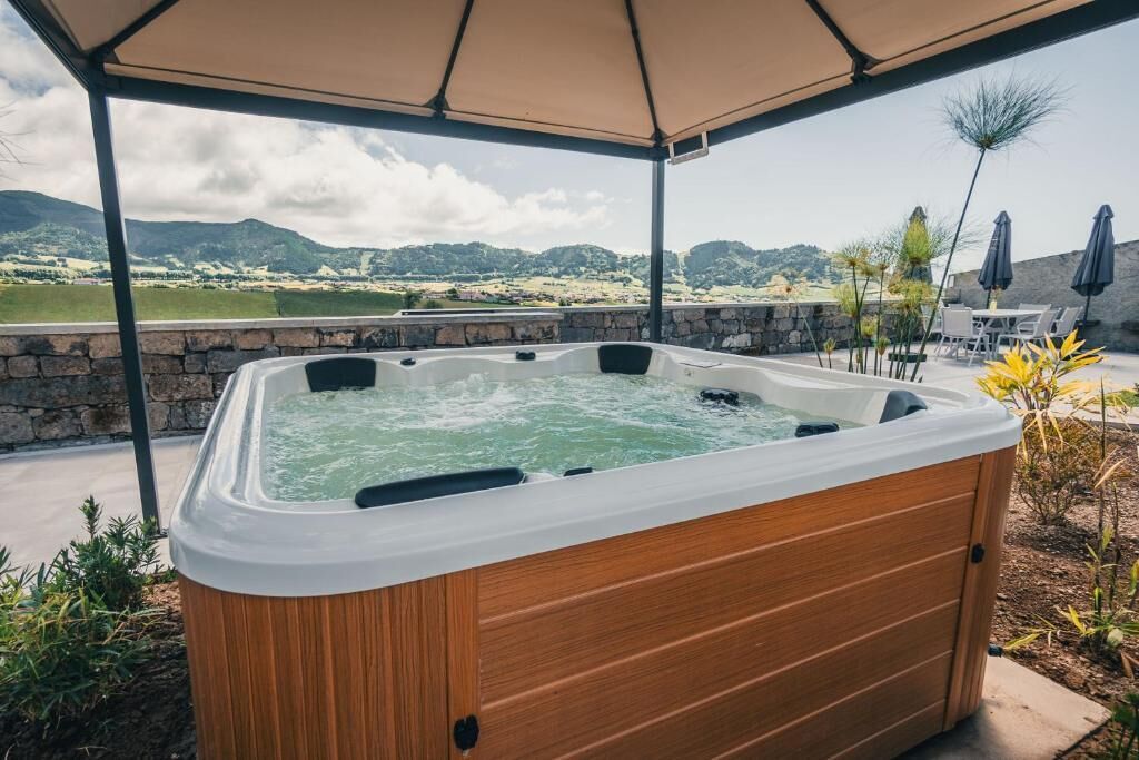 Un bain à remous en bois, installé sous une tonnelle et offrant une vue sur un paysage montagneux.