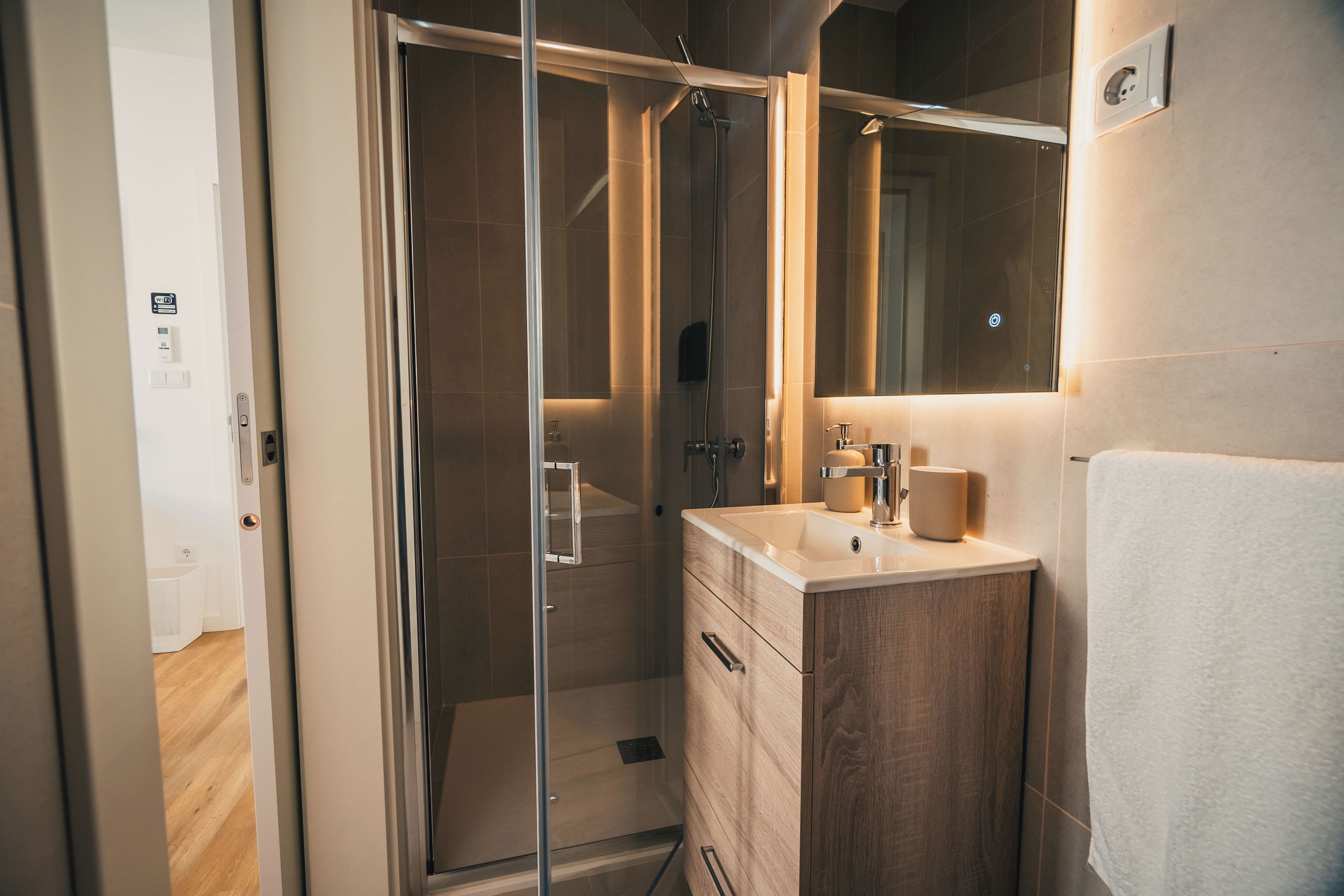Un baño moderno con ducha de vidrio, tocador de madera con lavamanos y un espejo sobre el tocador.