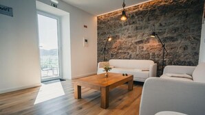 A modern living room with a stone wall, a wooden coffee table, and two white sofas. - Benilde Village House (Povoacao)