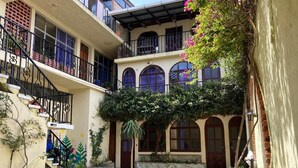 A courtyard with a two-story building, a staircase, and a small palm tree. - Kasa Kiwi Hostel and Travel (Quetzaltenango)