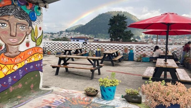 An outdoor patio with picnic tables, potted plants, and a mural on the wall. - Kasa Kiwi Hostel and Travel (Quetzaltenango)