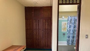 A small, enclosed bathroom with a wooden wardrobe, a wooden bench, and a shower curtain. - Kasa Kiwi Hostel and Travel (Quetzaltenango)