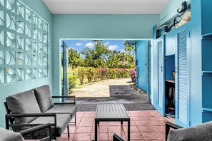 Un porche cubierto con sofá y mesa, vista a un jardín y taquillas azules.