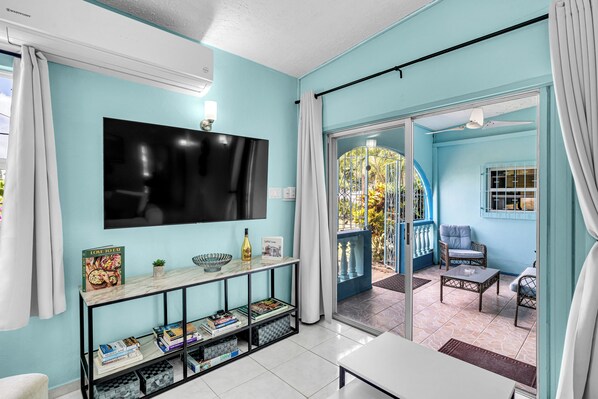 Una habitación con televisión, una consola con libros, un sofá y una mesa de comedor.