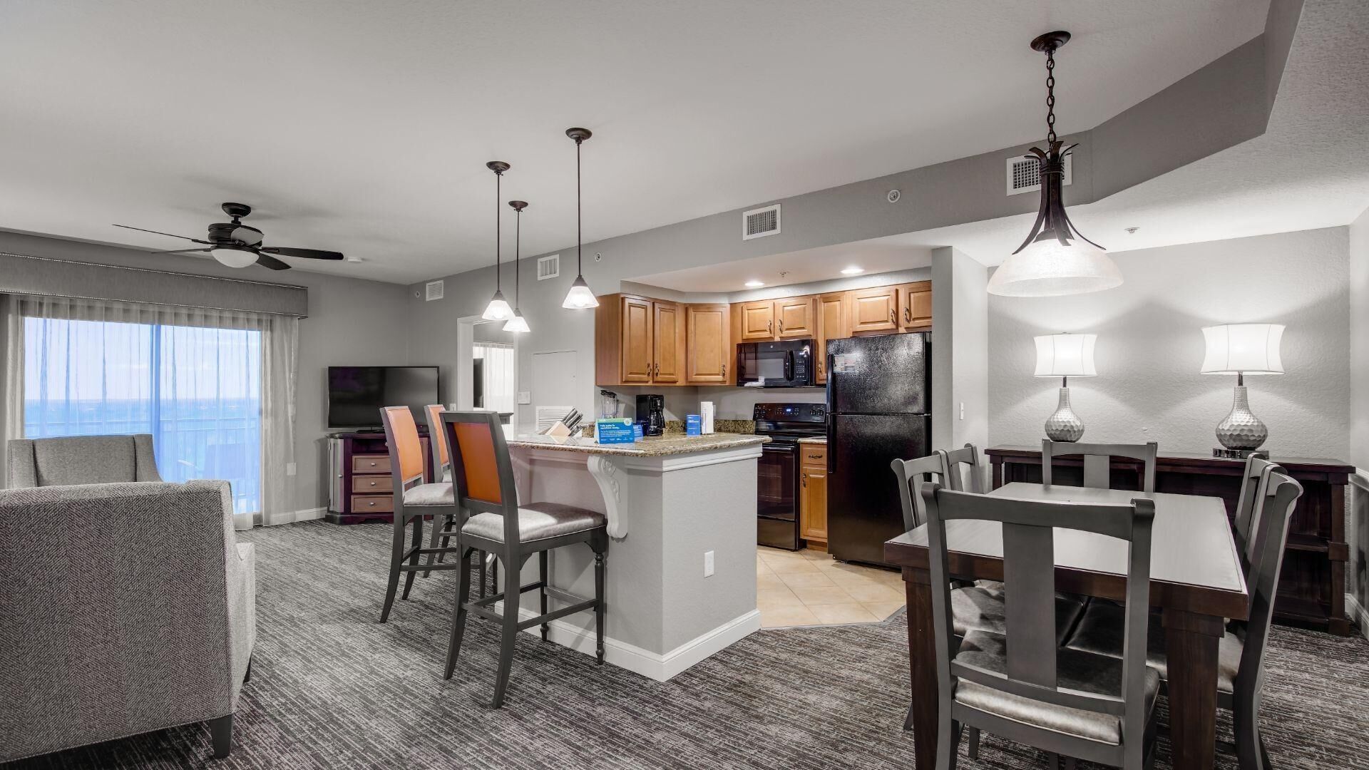 A modern hotel room with a dining area, kitchen, and a balcony with a view.
