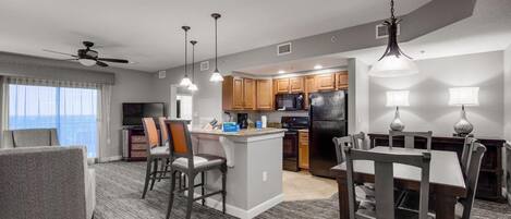 A modern hotel room with a dining area, kitchen, and a balcony with a view.