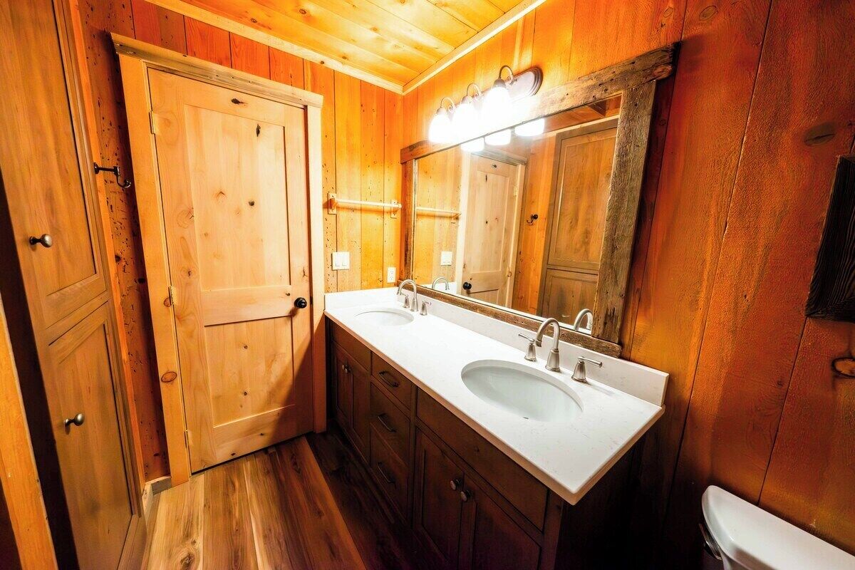 Un baño de madera con dos lavamanos, un espejo y un inodoro.