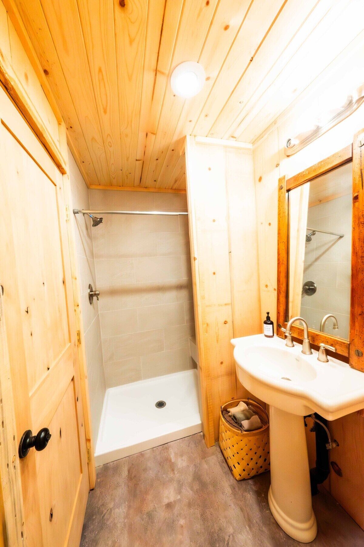 A wooden bathroom with a shower, a sink, and a mirror.