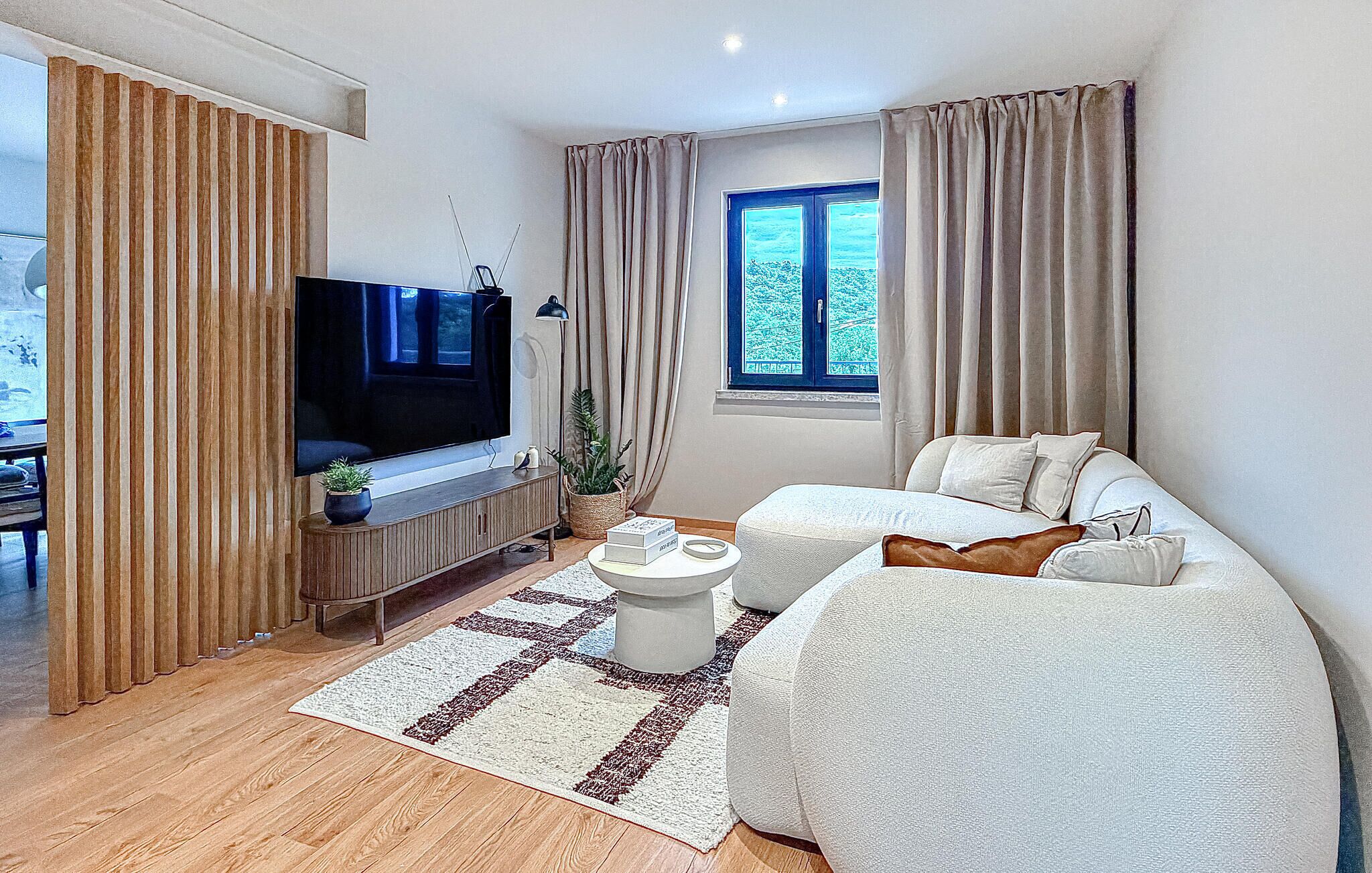 Un salon moderne avec un téléviseur à écran plat, un canapé, une table basse et une fenêtre avec des rideaux.