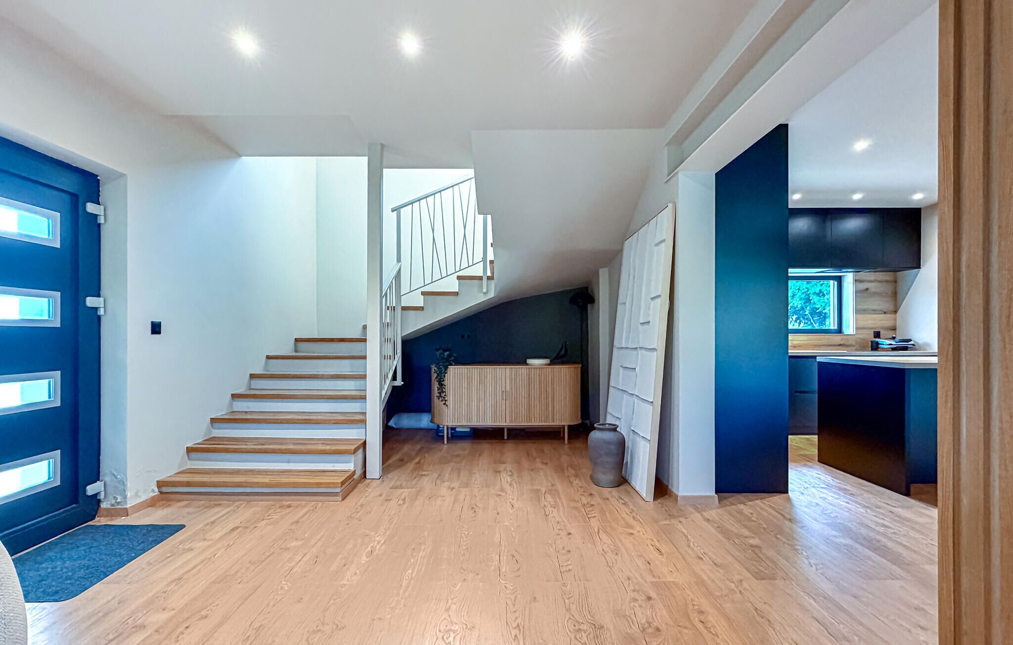 A modern interior with a wooden staircase, a kitchen area, and a dining space.