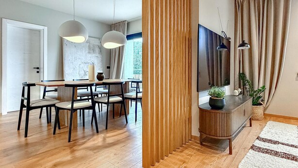 Een moderne woonkamer met een flatscreen televisie, houten meubels en een groot raam.