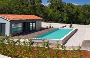 Ein modernes Haus mit Schwimmbad, Terrasse und Blick auf einen Wald.