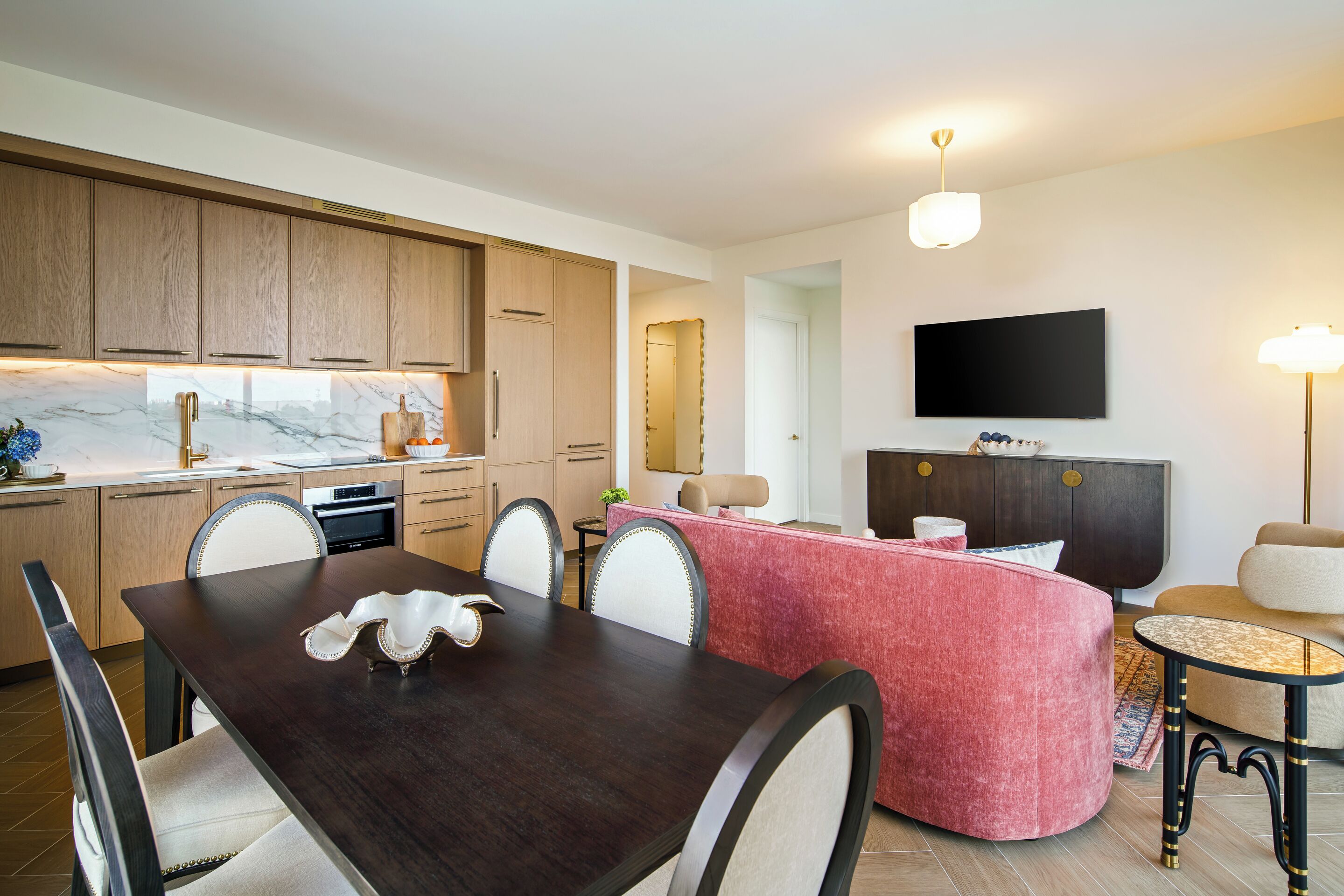 A modern kitchen with wooden cabinets, a marble countertop, and a dining area with a dark wooden table and white chairs.