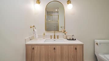 Een badkamer met een houten wastafelmeubel, een witte wasbak, gouden details en een grote spiegel.