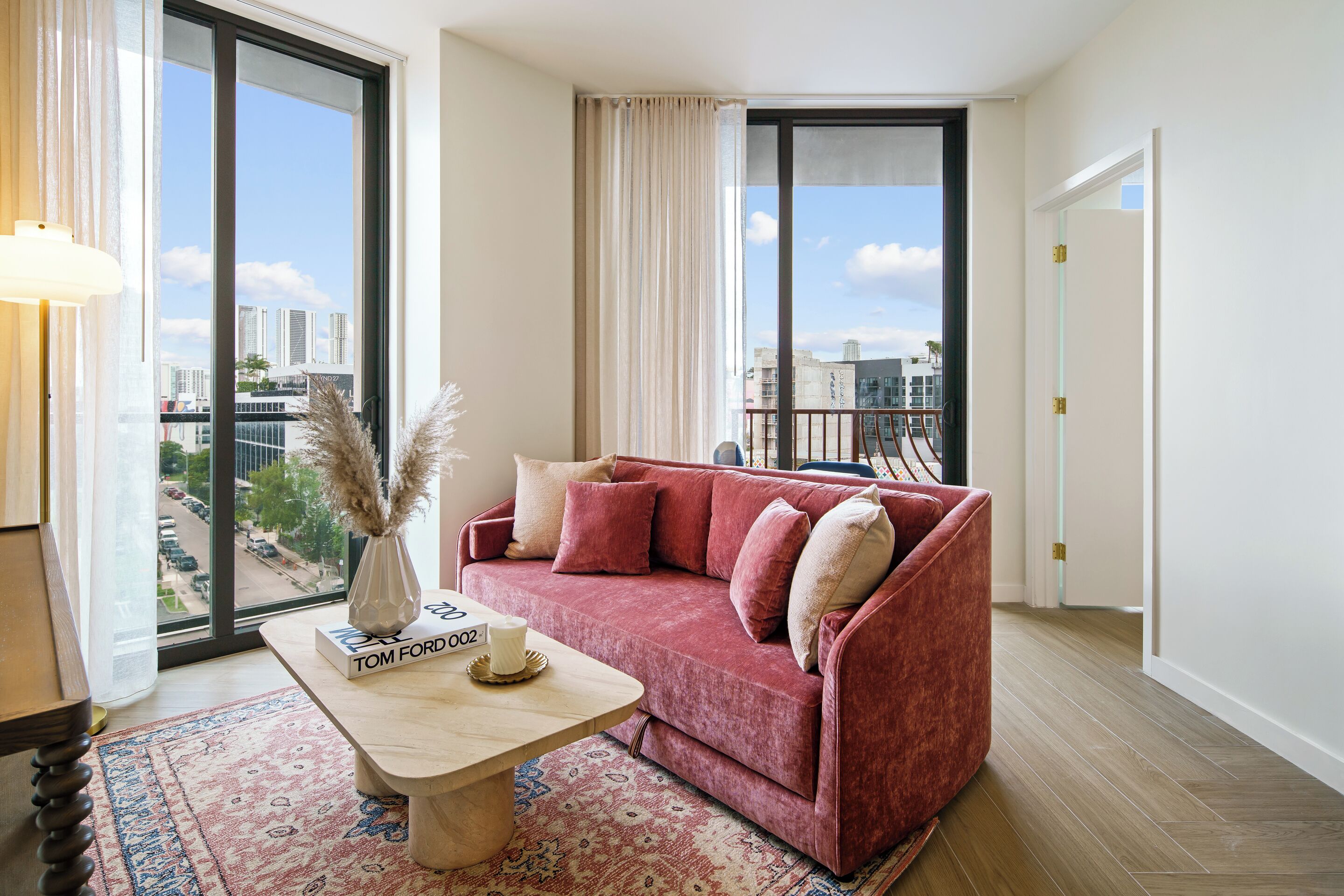 A modern living room with a red sofa, a coffee table, and a view of the city through large windows.