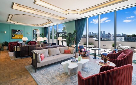 A modern living room with a sofa, armchairs, a coffee table, and a city view through large windows.