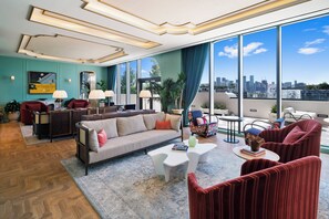 Una sala de estar moderna con sofá, sillones, una mesita de centro y vista a la ciudad a través de amplias ventanas.