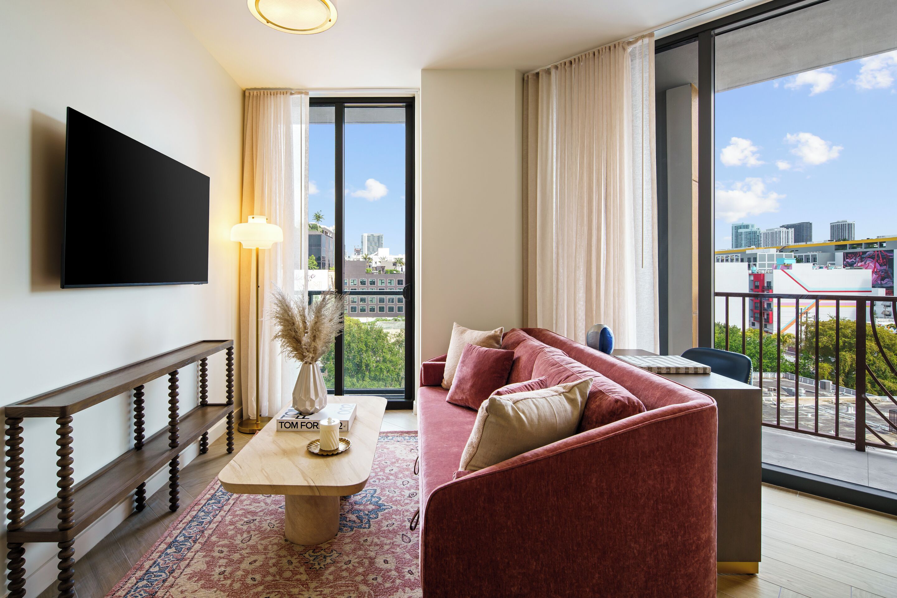 A modern living room with a sofa, a coffee table, a TV, and a large window with a city view.