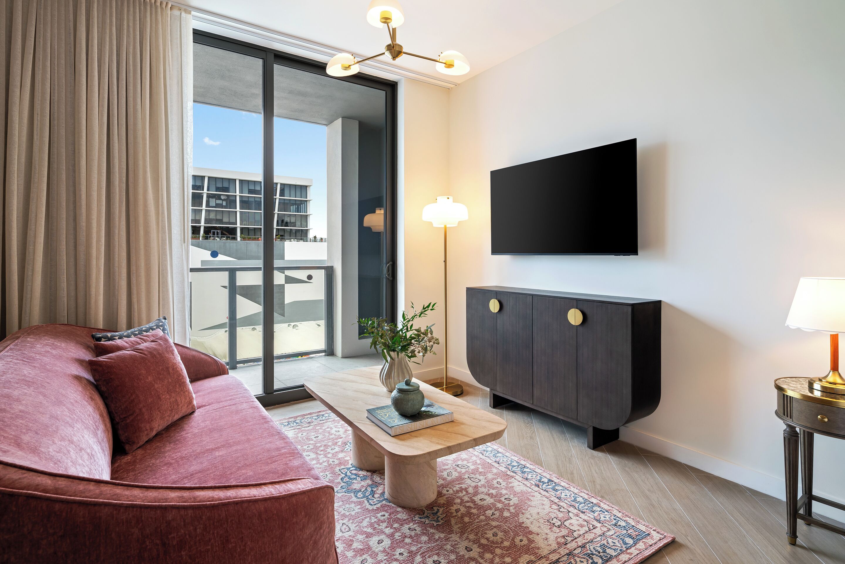 Un salon moderne comprenant un canapé, une table basse avec un livre et un vase, un téléviseur à écran plat, un meuble et un tapis à motifs.