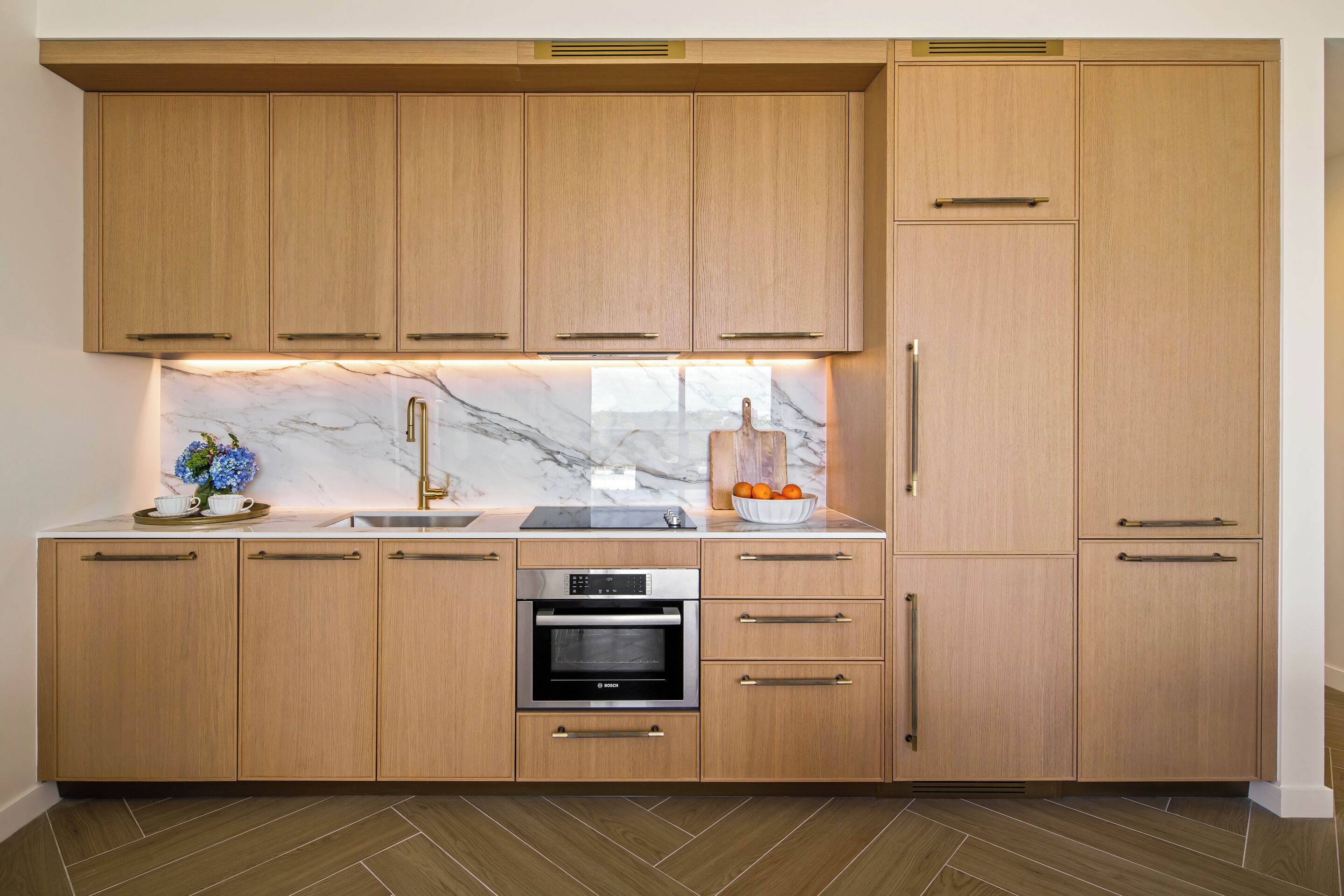 A modern kitchen with wooden cabinets, a built-in oven, and a marble backsplash.