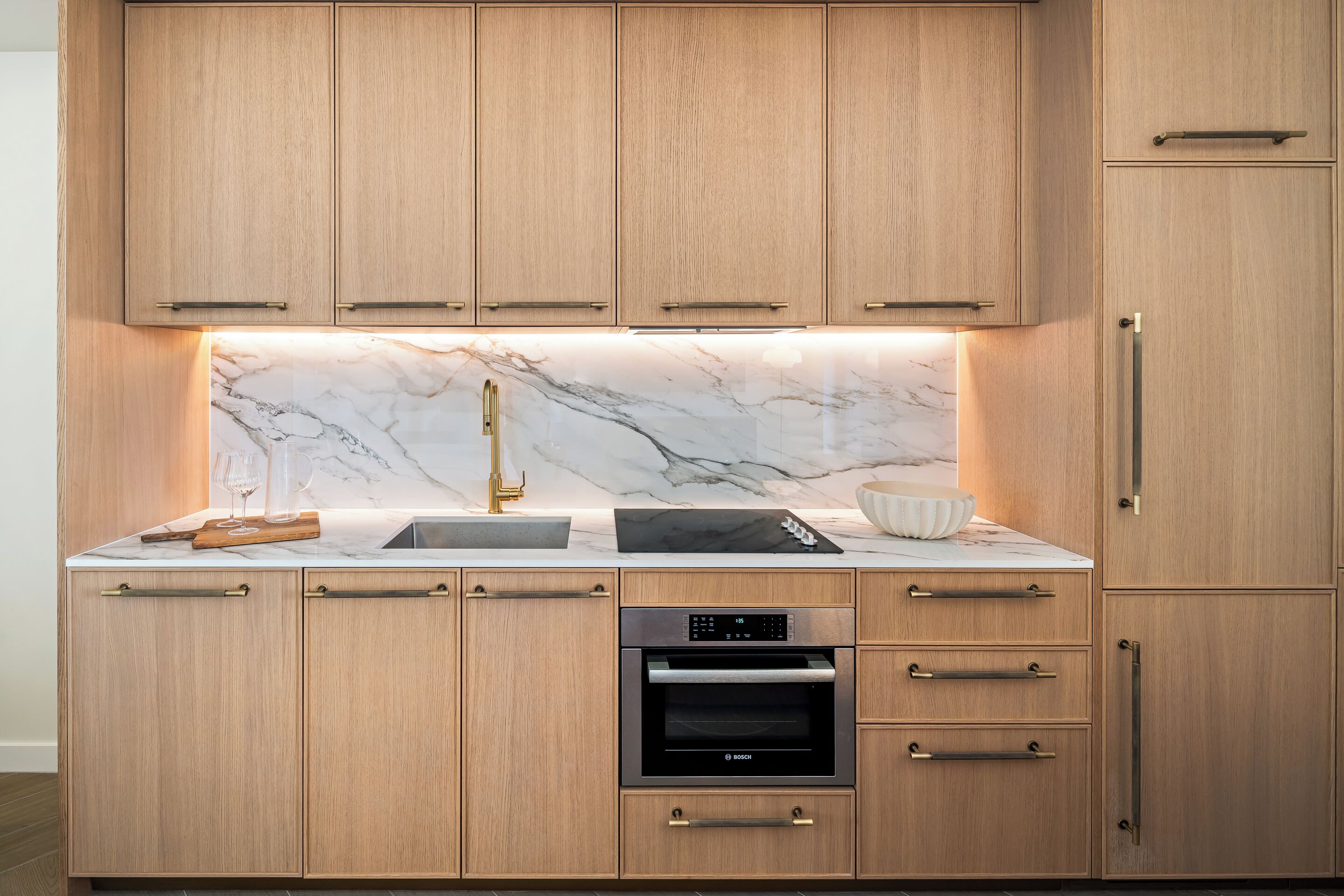 A kitchen with wooden cabinets, a marble backsplash, a Bosch oven, and a sink.