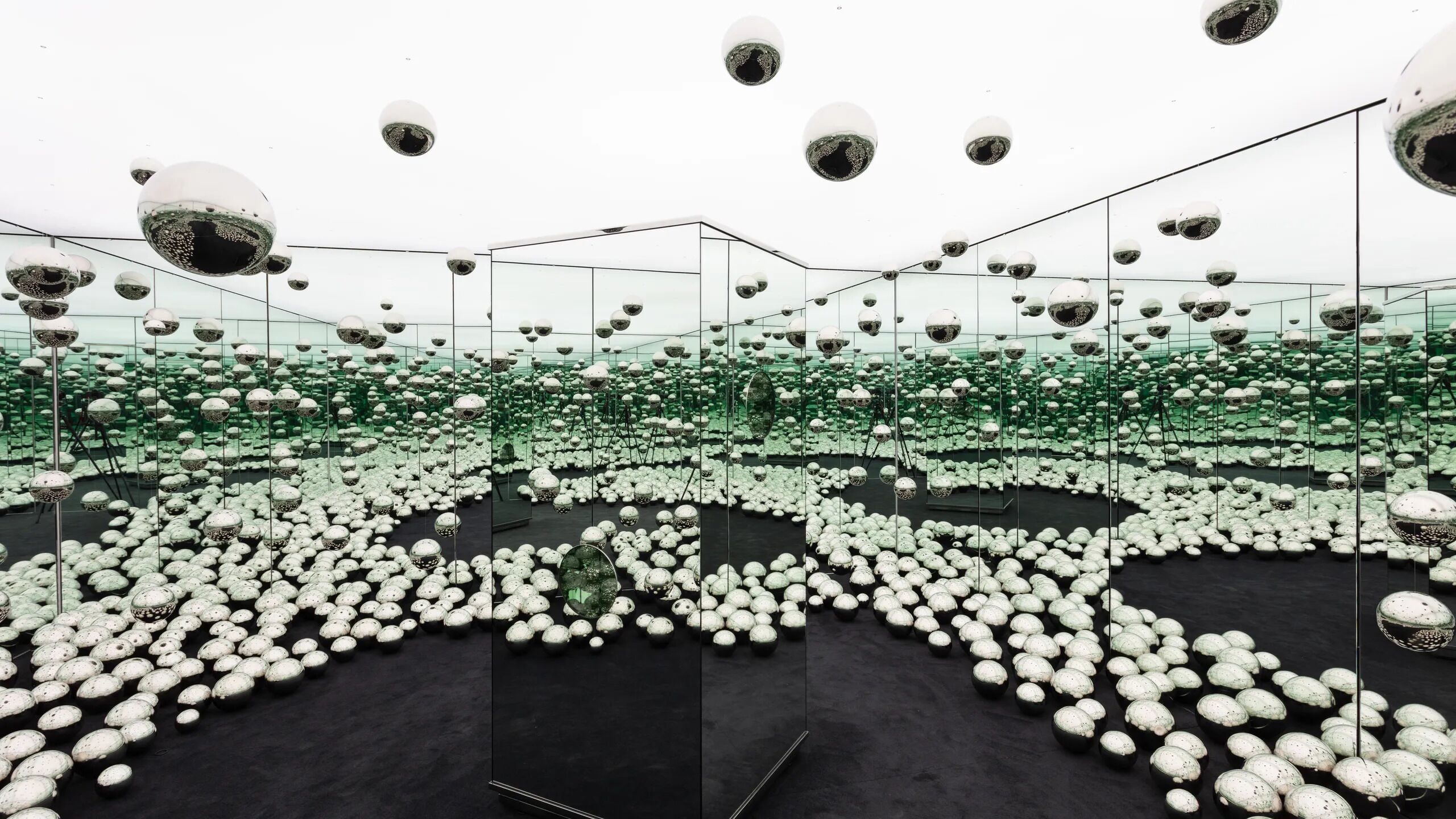 A room with a mirrored ceiling, multiple spherical objects on the floor, and a central black platform.