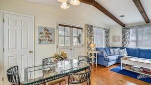 A dining area with a glass table and chairs, a blue sofa, and a patterned wall. - Classic 3BR House | Porch, Pool & Beach Nearby (Bethany Beach)