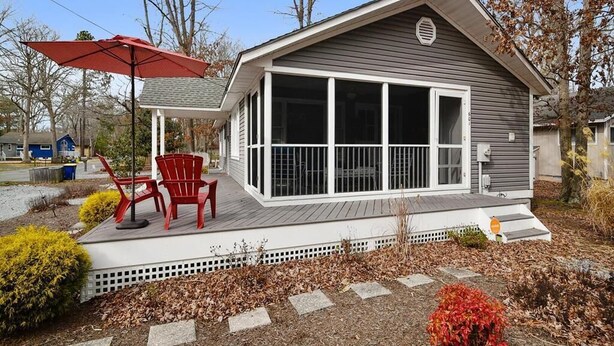 A single-story house with a covered porch, a sliding glass door, and a red umbrella. - Classic 3BR House | Porch, Pool & Beach Nearby (Bethany Beach)