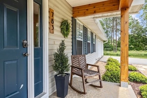 A house with a dark blue door, a wooden rocking chair, a potted tree, and a number sign on the wall. - Private Pickleball Court, Hot Tub and Fire Pit (Arden)
