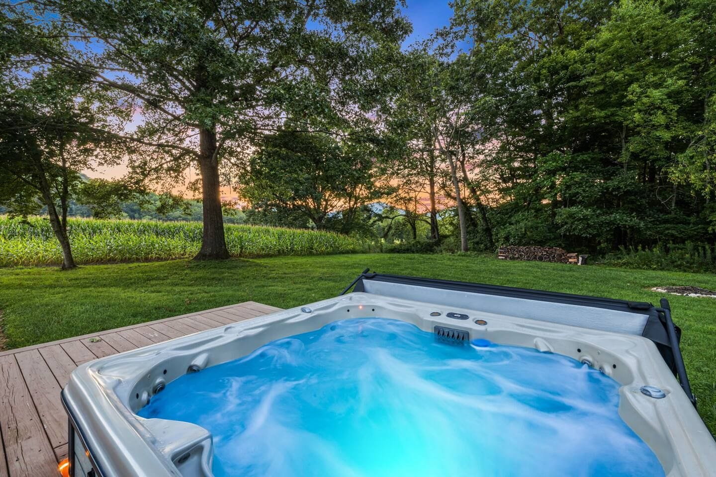 Ein Whirlpool in einem Garten mit Holzterrasse, umgeben von üppigem Grün und Bäumen.