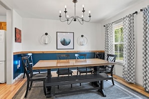 A dining room with a wooden table, black chairs, a chandelier, framed artwork, and patterned curtains. - Private Pickleball Court, Hot Tub and Fire Pit (Arden)