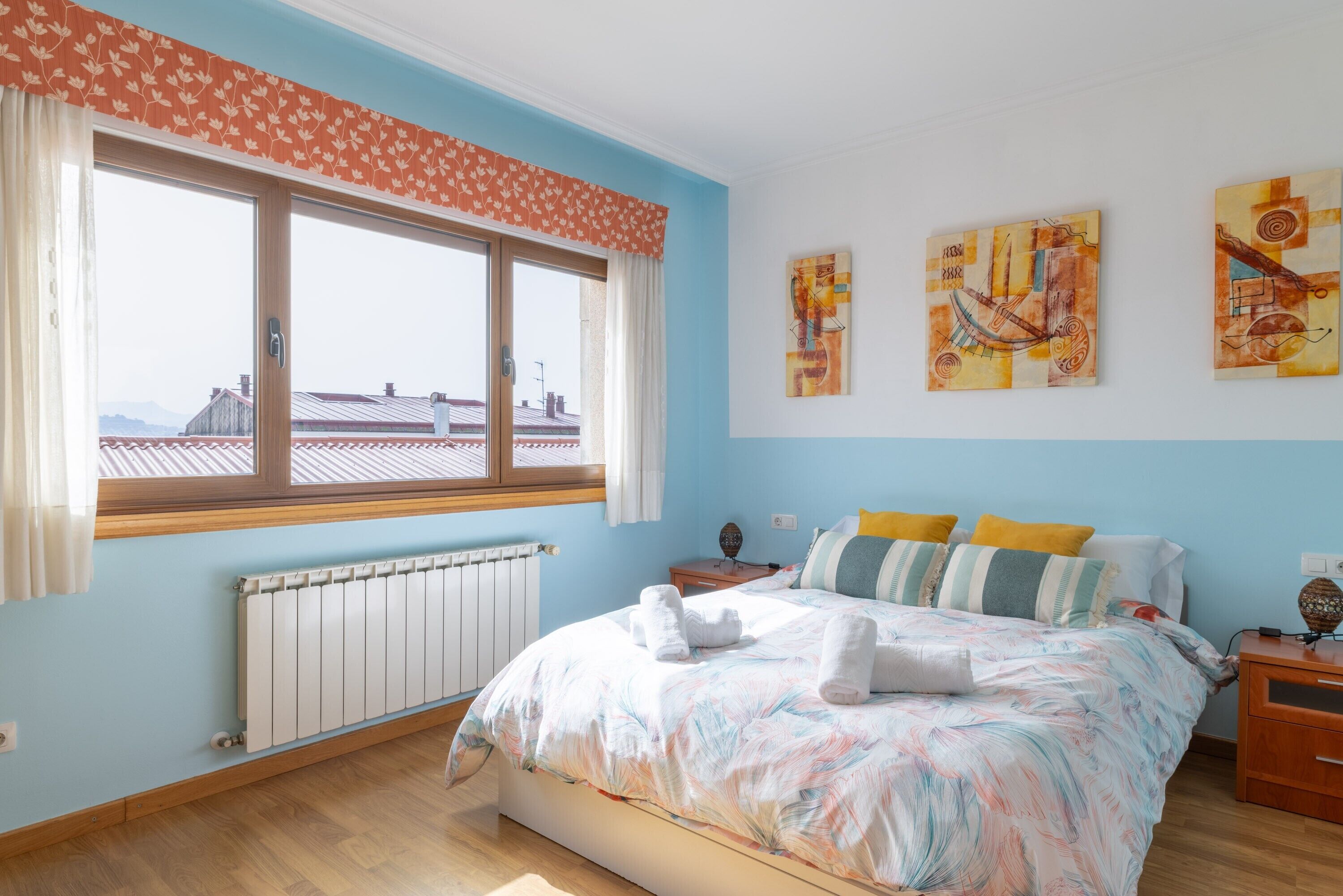 A bedroom with a large window, a bed with towels, a radiator, and abstract wall art.